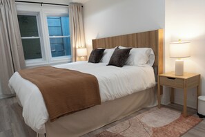 A neatly made bed with a brown blanket, a wooden headboard, bedside lamps, and a window with curtains. - A stylish retreat in Mount Pleasant, one of DC's most walkable neighborhoods. Two bedrooms plus a sofa bed sleep six, with two full baths - plus the city's rarest luxury: your own private off-street parking. Walk to Metro, cafes & Zoo. (Washington)
