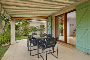 Un patio al aire libre con mesa y sillas, una pérgola arriba y un ventanal corredizo que da a un espacio interior.