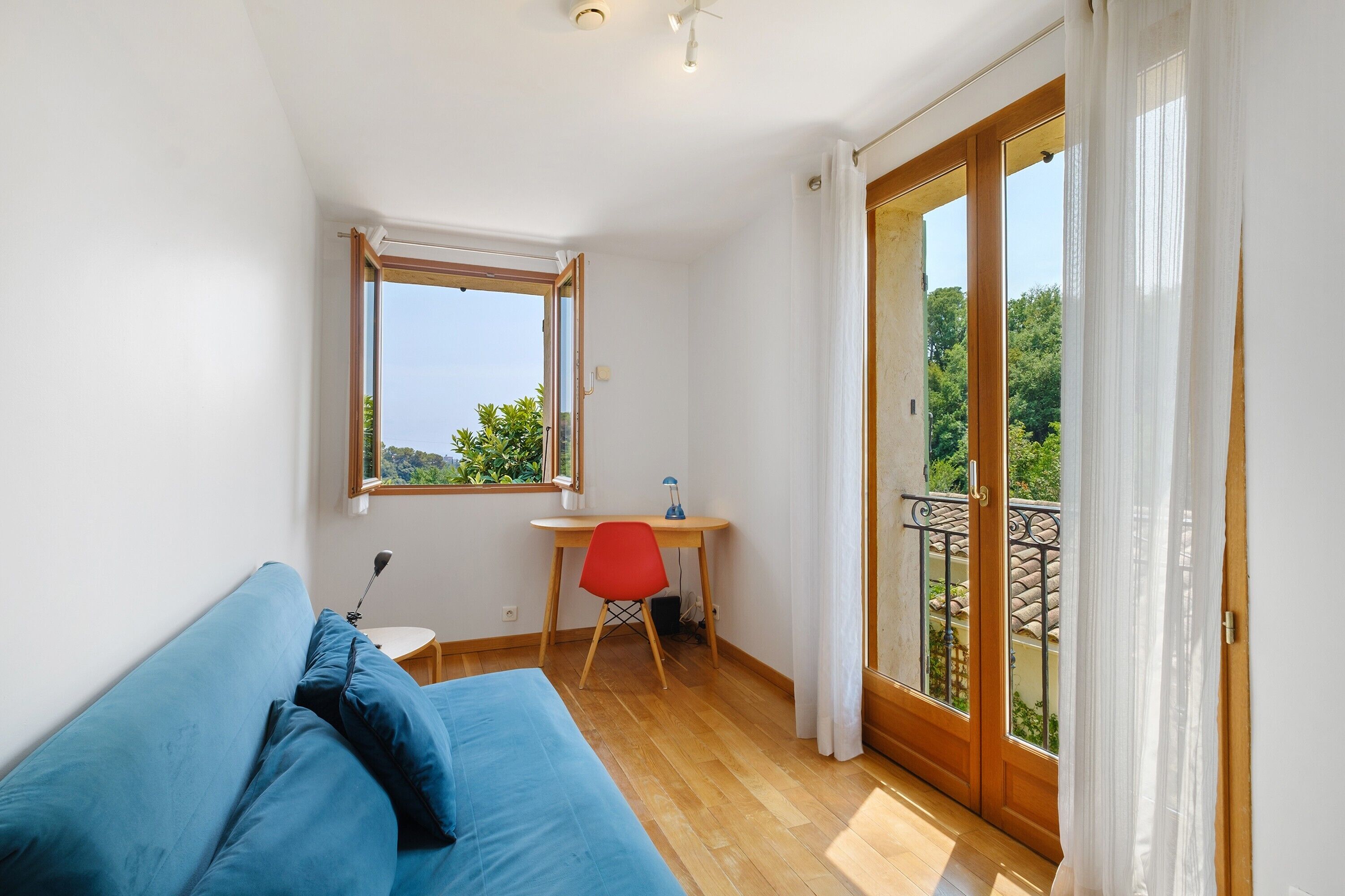 A room with a bed, a desk, a chair, and a balcony with a view.