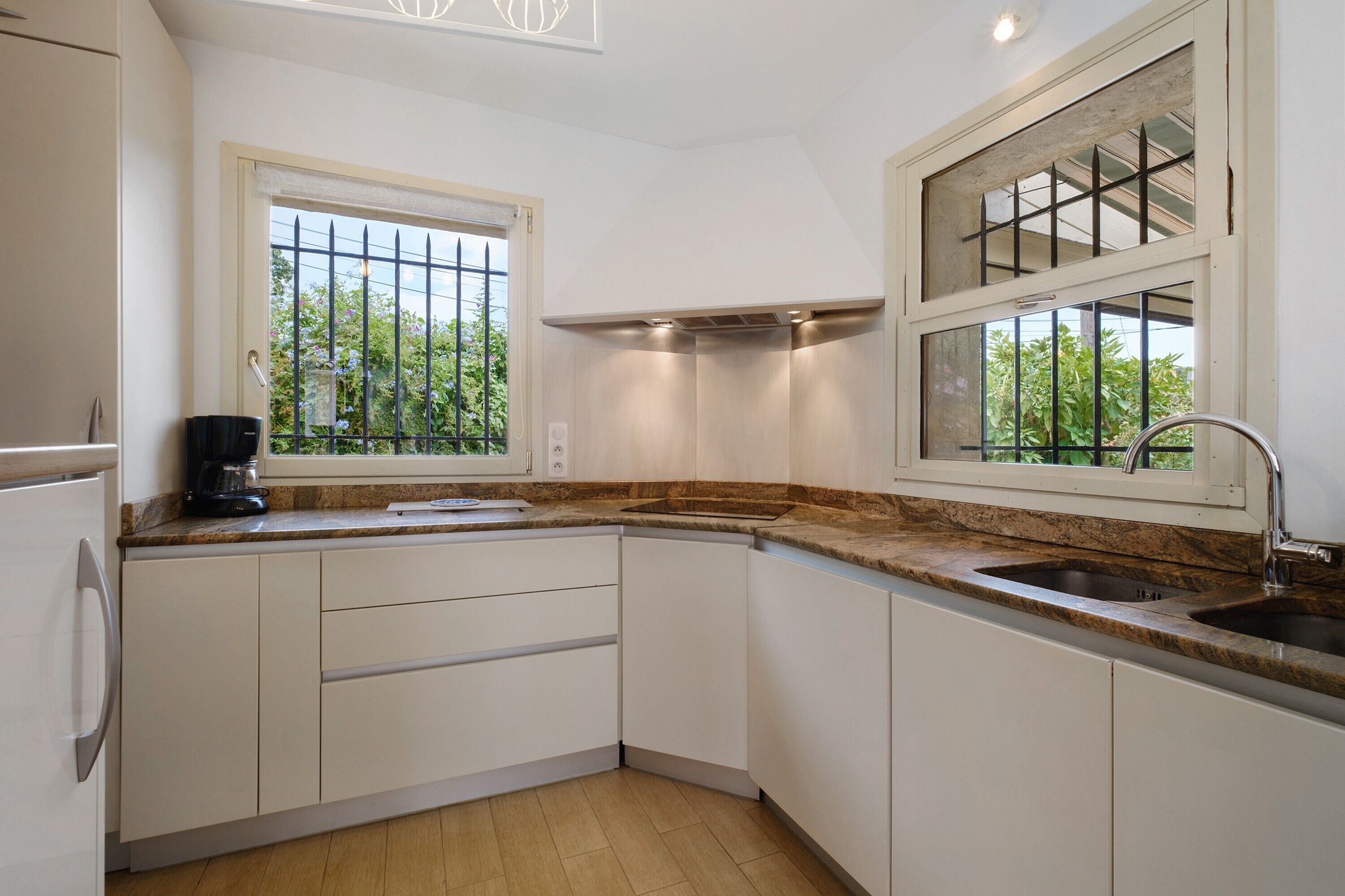 A kitchen with white cabinets, a granite countertop, a coffee maker, and a window with a view of greenery.