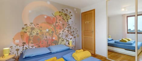 Un dormitorio con una cama grande, una mesita de noche con lámpara, un espejo y una pared decorada con un mural floral.