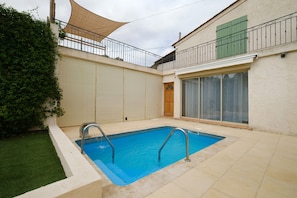 Una piscina rectangular con escalera metálica, rodeada por un patio empedrado.
