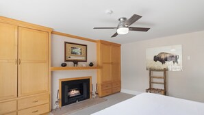 Ein Schlafzimmer mit einem Bett, einem Kamin, Holzschränken, einem Deckenventilator und einem Bild an der Wand.