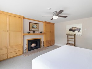 Ein Schlafzimmer mit einem Bett, einem Kamin, Holzschränken, einem Deckenventilator und einem Bild an der Wand.