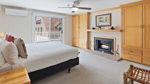 Ein Schlafzimmer mit einem Bett, einem Kamin, Holzschränken, einem Deckenventilator und Blick durch ein Fenster.