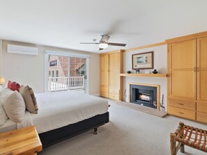 Ein Schlafzimmer mit einem Bett, einem Kamin, Holzschränken, einem Deckenventilator und Blick durch ein Fenster.