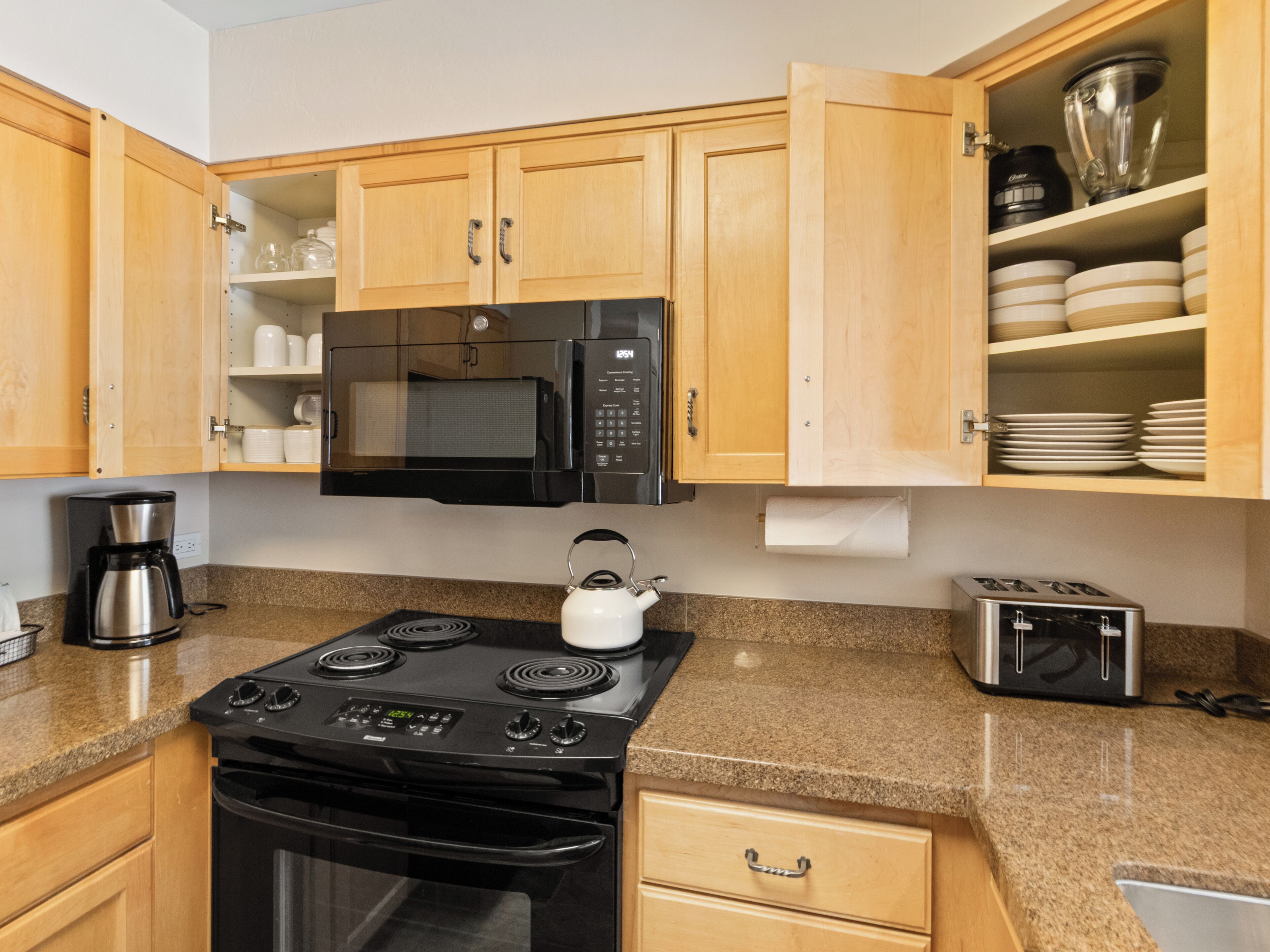 A kitchen with wooden cabinets, a microwave, a stove, a kettle, a coffee maker, and a toaster.