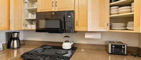 Una cocina con armarios de madera, microondas, estufa, hervidor, cafetera y tostadora.