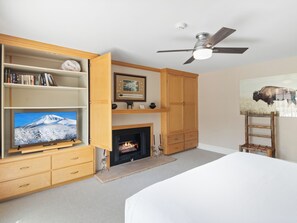 Une chambre à coucher avec un lit, une cheminée, un téléviseur et un ventilateur de plafond.