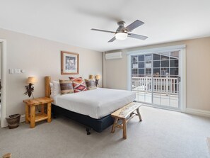 Une chambre à coucher avec un lit, des lampes de chevet, un ventilateur de plafond, une fenêtre donnant sur un beau paysage et un petit banc en bois.