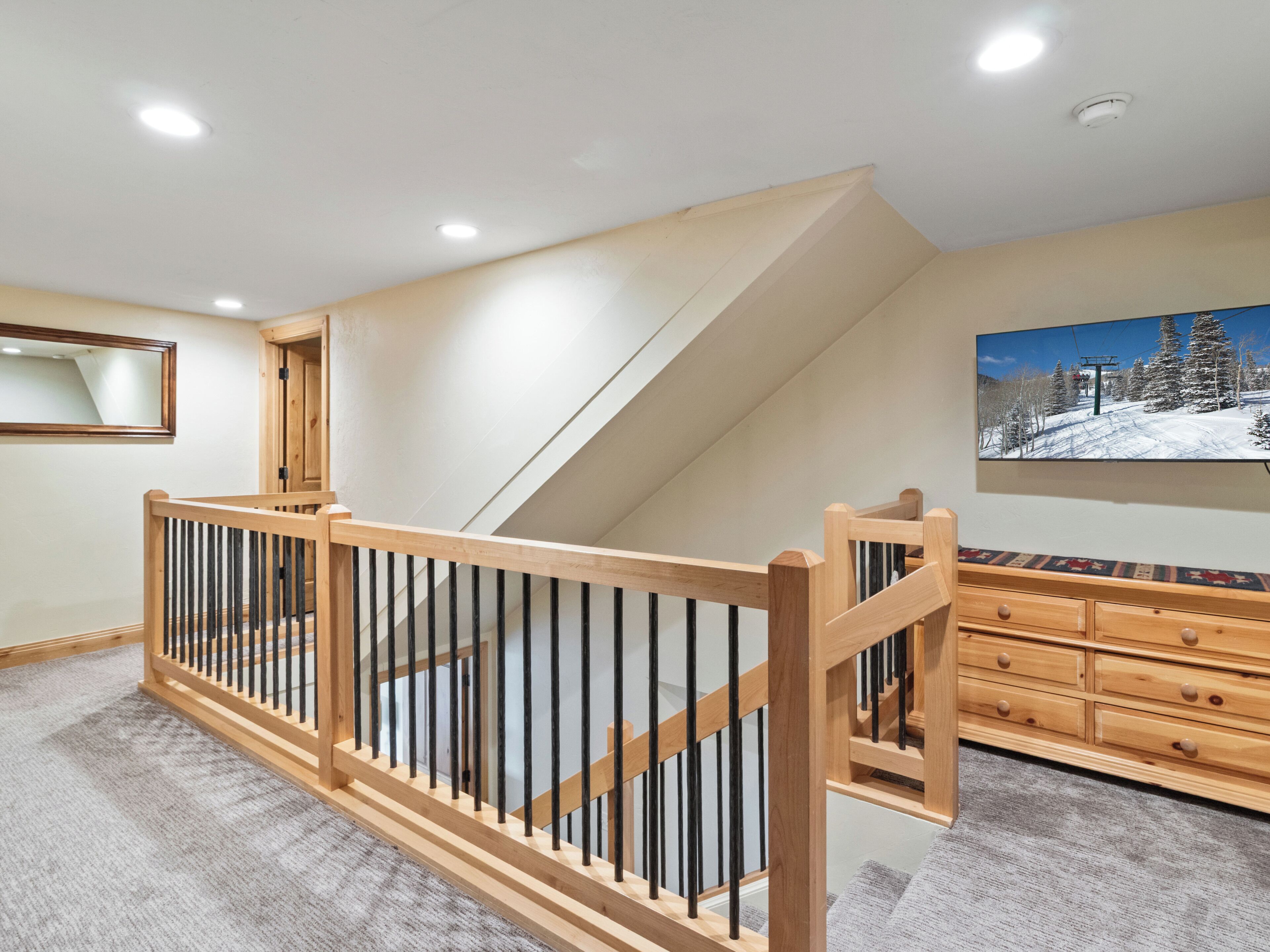 A room with a wooden staircase, a flat-screen TV, and a ski-themed painting.