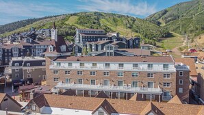 Un edificio de varios pisos con una torre destacada, rodeado de otros edificios residenciales, con colinas verdes al fondo.