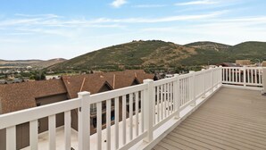 Una terraza de madera con barandillas blancas que da vista a una zona residencial con casas y colinas al fondo.