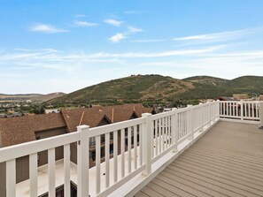 Eine Holzterrasse mit weißen Geländern, mit Blick auf eine Wohngegend mit Häusern und Hügeln im Hintergrund.