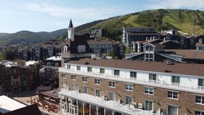 A multi-story building with a prominent tower, a covered outdoor seating area, and a view of a hilly landscape in the background. - Resort Center 5058 | Amazing Ski-In/Ski-Out with Mountain Views & Pool Access (Park City)