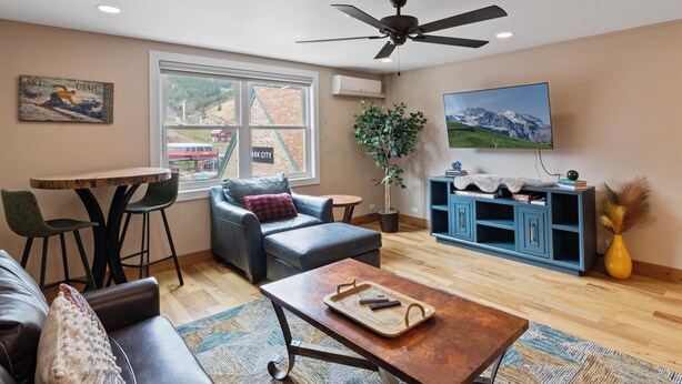 A living room with a sofa, a coffee table, a TV, a ceiling fan, a window with a view, and a plant. - Resort Center 5058 | Amazing Ski-In/Ski-Out with Mountain Views & Pool Access (Park City)
