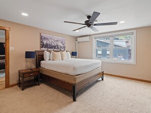 Un dormitorio con cama, ventilador de techo, ventana y un cuadro en la pared.