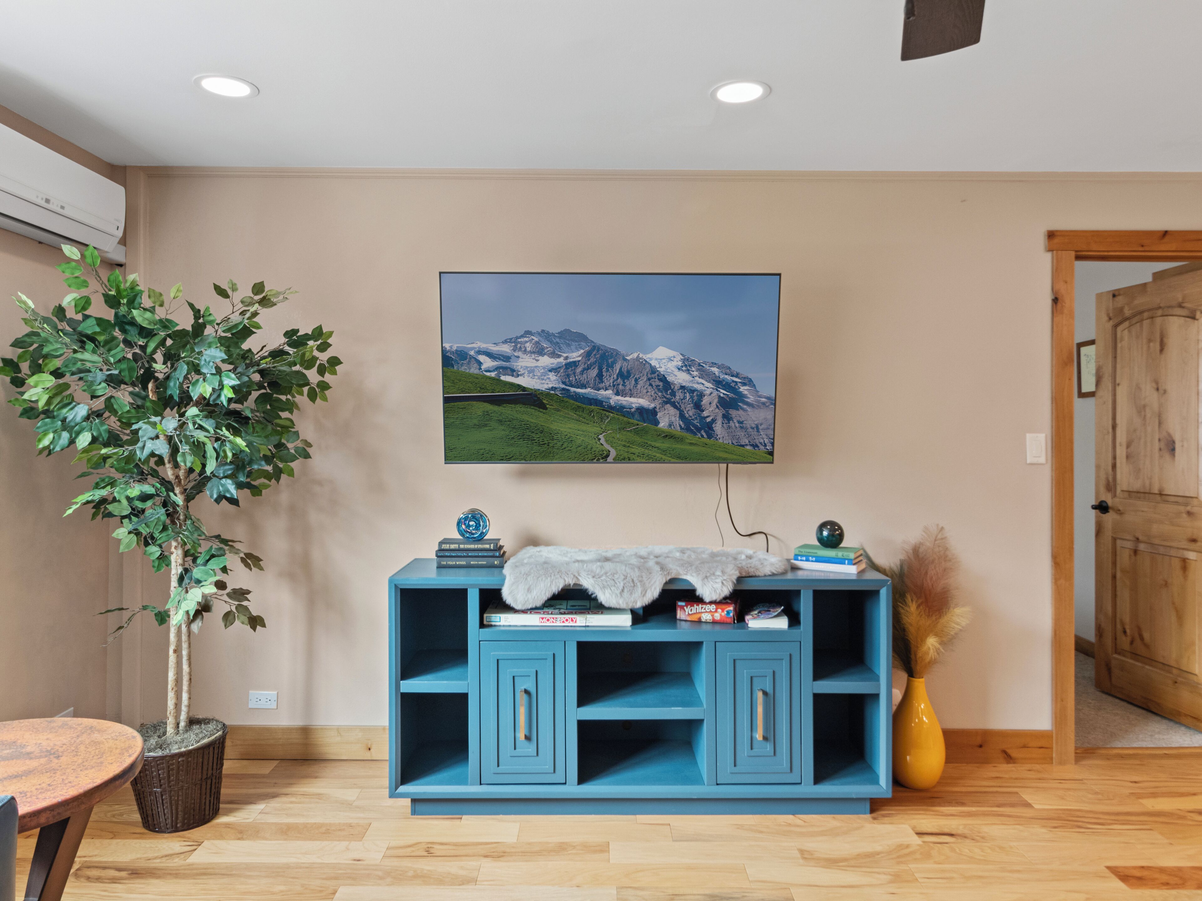 Een kamer met een houten vloer, een blauwe kast met boeken, een potplant en een ingelijste foto aan de muur.