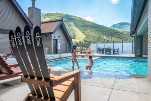 A swimming pool with a view of a mountain. There are Adirondack chairs and a table with chairs around the pool. - Resort Center 5058 | Amazing Ski-In/Ski-Out with Mountain Views & Pool Access (Park City)