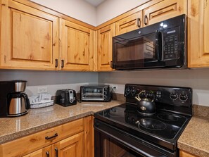 Una cocina con armarios de madera, microondas, tostadora, cafetera y estufa.