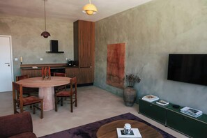 A modern living room with a round wooden dining table, a sofa, and a television mounted on the wall. - Stylish Boavista King Bed Studio - Casa da Musica (Porto)