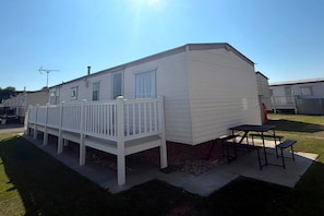 Una casa móvil con una terraza cercada y una mesa de picnic.