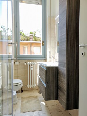 A modern bathroom with a toilet, a glass shower enclosure, a radiator, and a window. - Casa Milano | Metro in 2 steps | Direct to the Duomo & Linate (Milano)