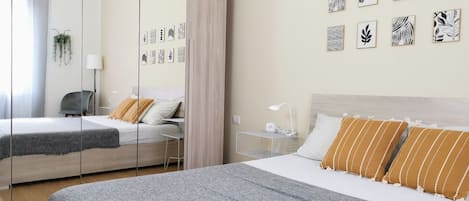 Un dormitorio moderno con dos camas, una mesita de noche con lámpara, un espejo y decoración en la pared.