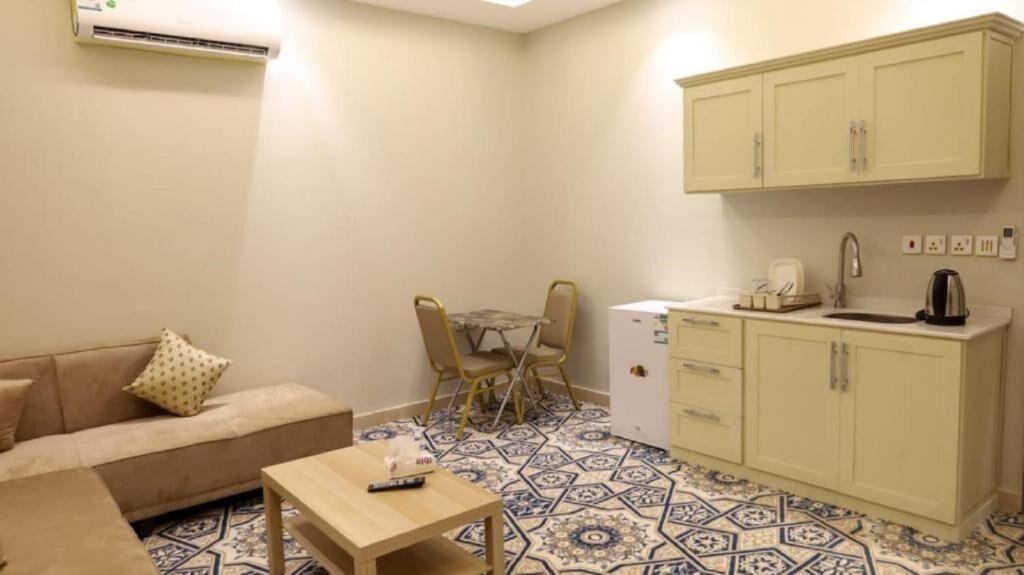Un espacio habitable compacto con kitchenette, un área de comedor con mesa y sillas, y un sofá sobre un piso con diseño.