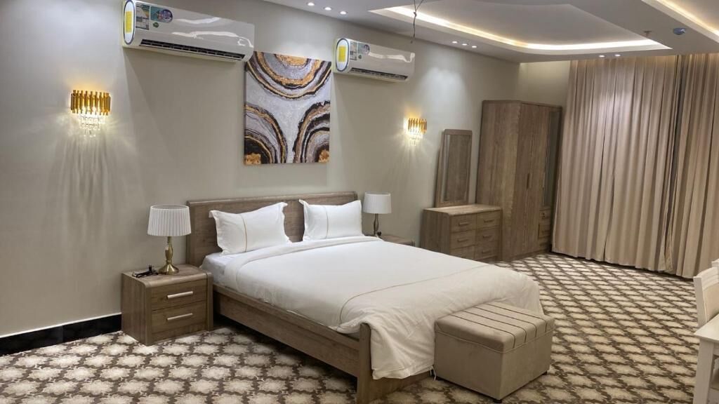 A modern bedroom with a large bed, bedside tables, a wardrobe, and a decorative wall piece.