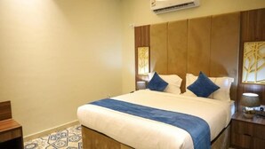 Quarto de hotel com cama, cabeceira de madeira, mesas de cabeceira e piso estampado.