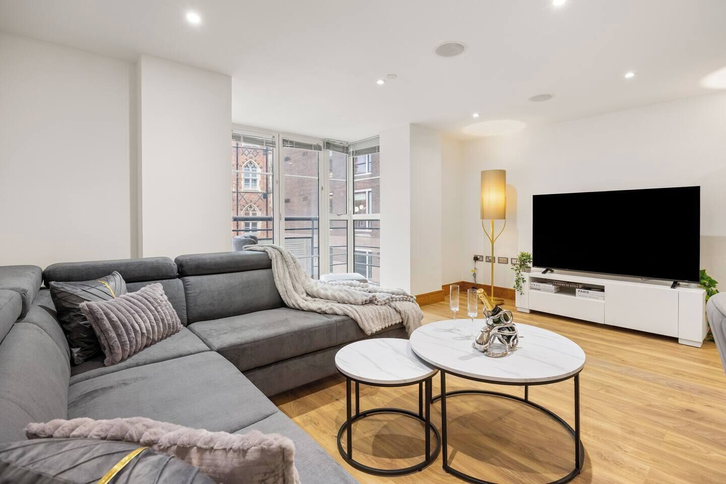A modern living room with a grey sofa, a white coffee table, and a flat-screen TV on a white cabinet.