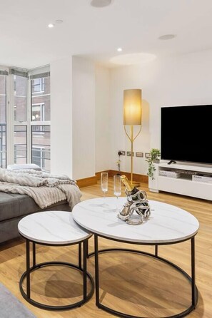 Ein modernes Wohnzimmer mit einer Couch, zwei runden Tischen, einem Fernseher und einem großen Fenster.