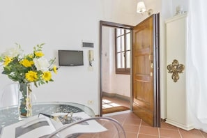 A room with a glass table, a vase with flowers, a television, and a wooden door. - UR NEST Window on Arno - one-bedroom apartment with view (Firenze)