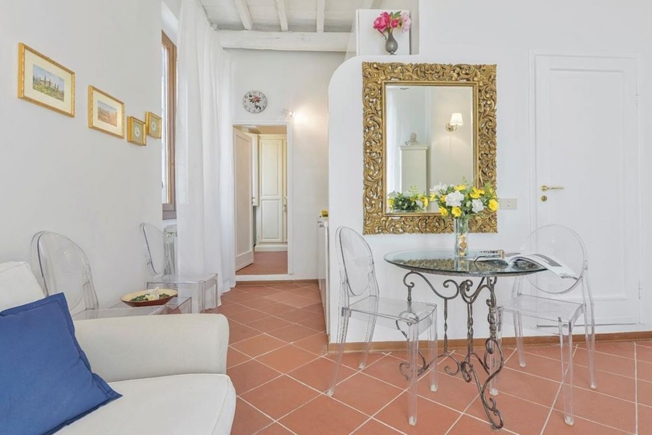 A room with a white sofa, a dining table with chairs, a mirror with a gold frame, and a door.