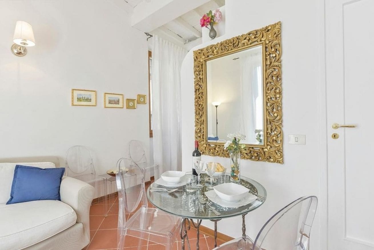 Una habitación moderna con un sofá blanco, una mesa de comedor de vidrio y un espejo grande y decorativo.