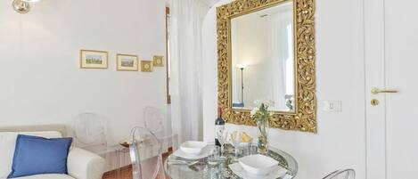 Una habitación moderna con un sofá blanco, una mesa de comedor de vidrio y un espejo grande y decorativo.
