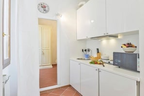 A kitchen with white cabinets, a microwave, a bowl of fruit, and a clock on the wall. - UR NEST Window on Arno - one-bedroom apartment with view (Firenze)