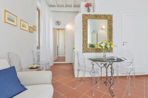 A room with a white sofa, a dining table with chairs, a mirror with a gold frame, and a door. - UR NEST Window on Arno - one-bedroom apartment with view (Firenze)