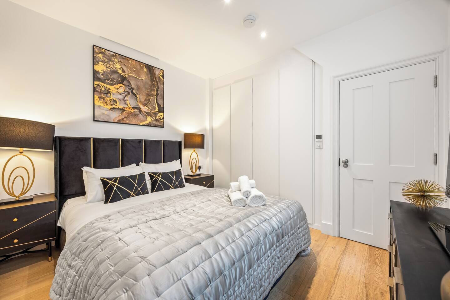 Een slaapkamer met een bed, twee nachtkastjes, een schilderij en een deur.