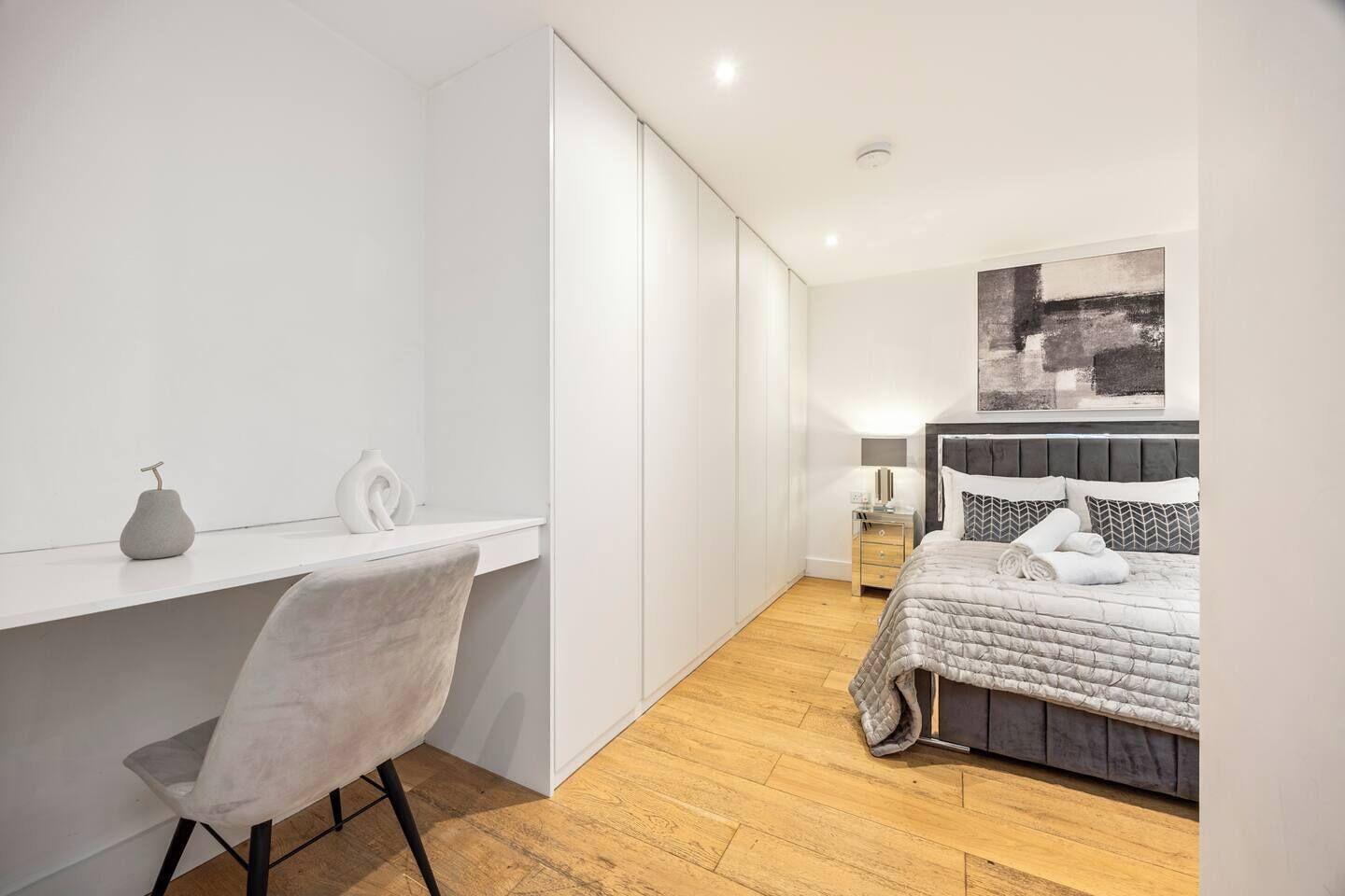 A modern bedroom with a bed, bedside table, lamp, and a desk with chair.