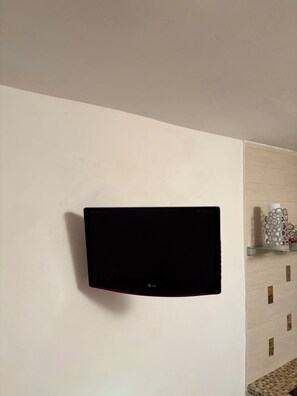 Un téléviseur à écran plat fixé au mur dans une pièce dont le mur est recouvert de carreaux et qui comporte une petite étagère avec des objets décoratifs.