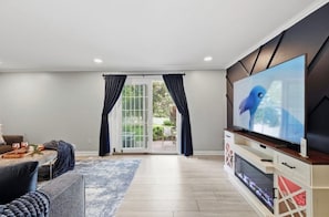 Ein Wohnzimmer mit Flachbildfernseher, einer Couch, einem Couchtisch und einer Glastür, die auf eine Terrasse führt.