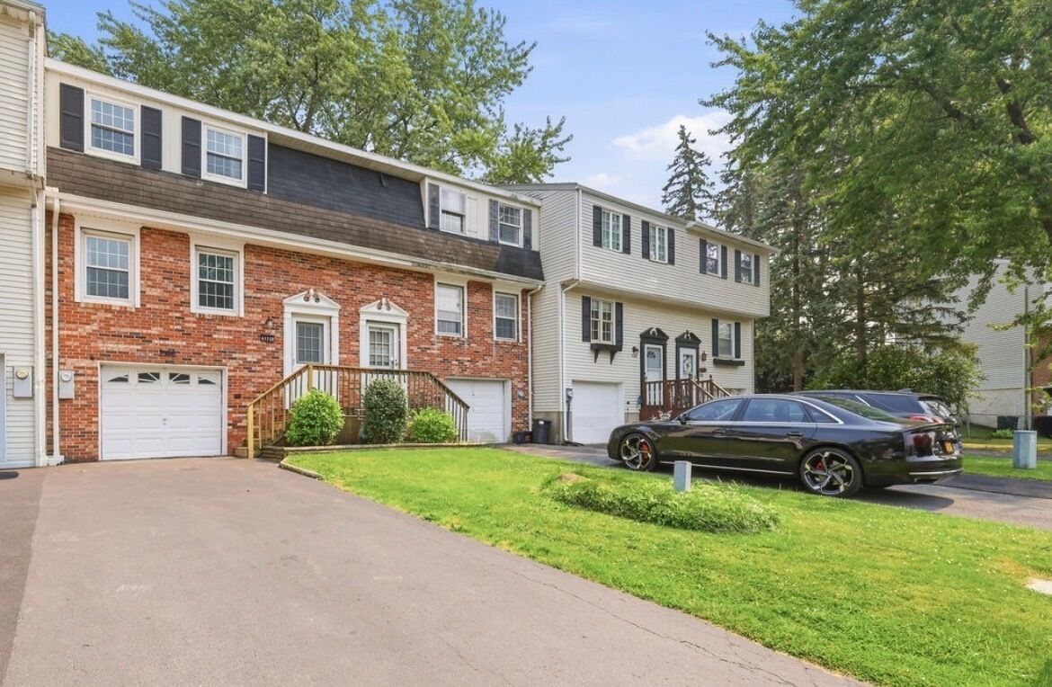 A two-story residential building with a brick facade, a garage, and a driveway.