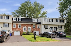 A two-story apartment building with a brick facade, a garage, and a parking area with cars.