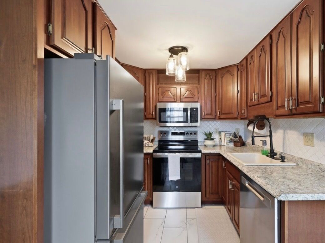A kitchen with wooden cabinets, stainless steel appliances, a granite countertop, and a pendant light fixture.