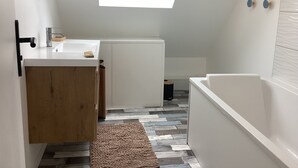 A compact bathroom with a skylight, a white sink, a wooden cabinet, and a white bathtub. - A 5-minute walk from Port Bail Beach: house with an enclosed garden. (Port-Bail-sur-Mer)