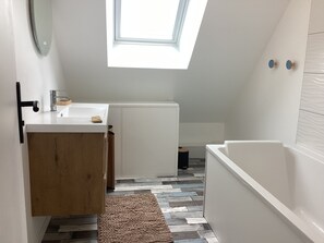 Ein kleines Badezimmer mit Oberlicht, einem weißen Waschbecken, einem Holzschrank und einer weißen Badewanne.