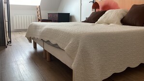 A bedroom with a bed, a radiator, a chair, and a wall with a floral painting. - A 5-minute walk from Port Bail Beach: house with an enclosed garden. (Port-Bail-sur-Mer)