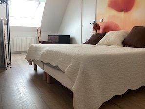 Ein Schlafzimmer mit einem Bett, einem Heizkörper, einem Sessel und einer Wand mit einem Blumenbild.